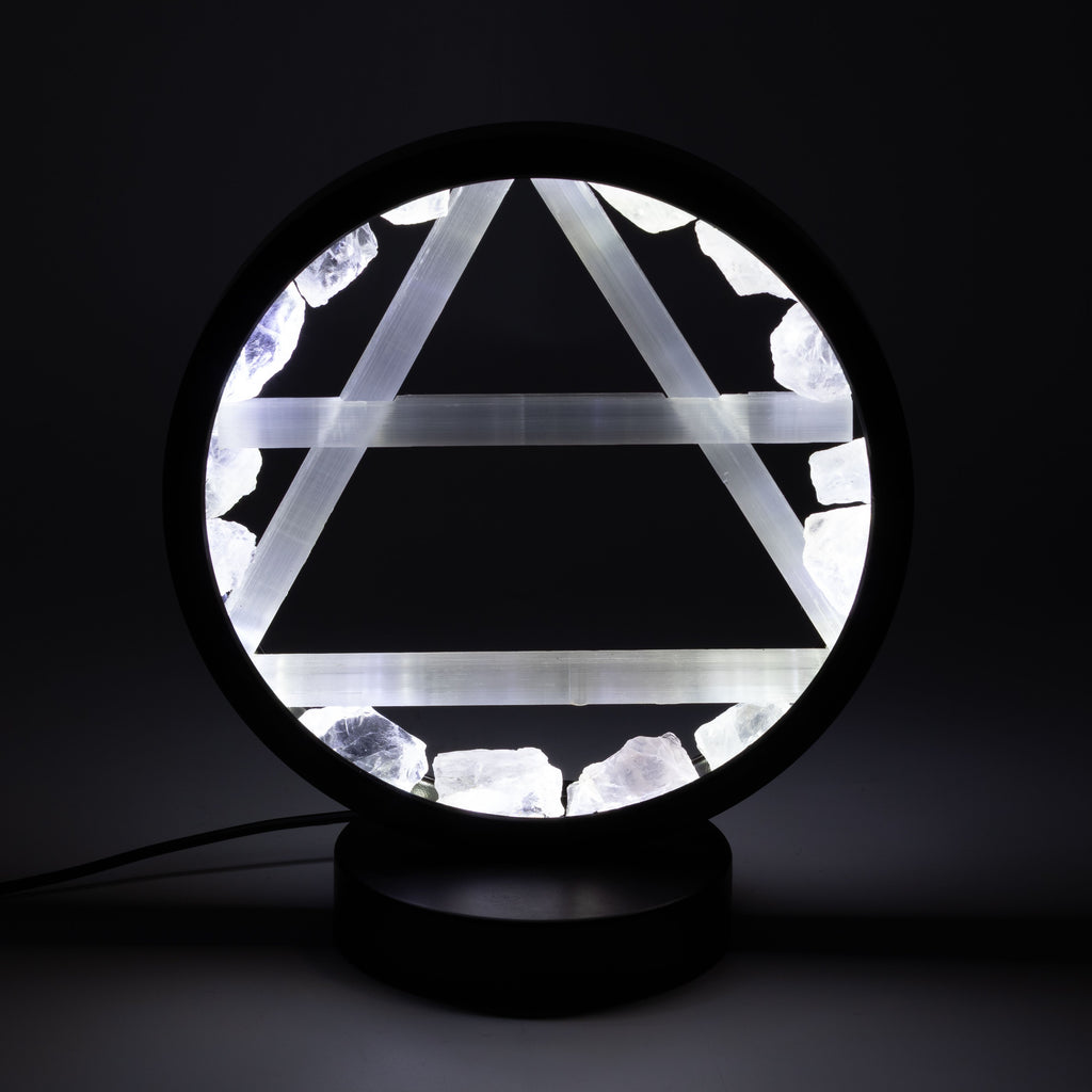 A circular black table lamp with a glowing white geometric triangle design and rough white crystal-like accents, shown on a dark background.