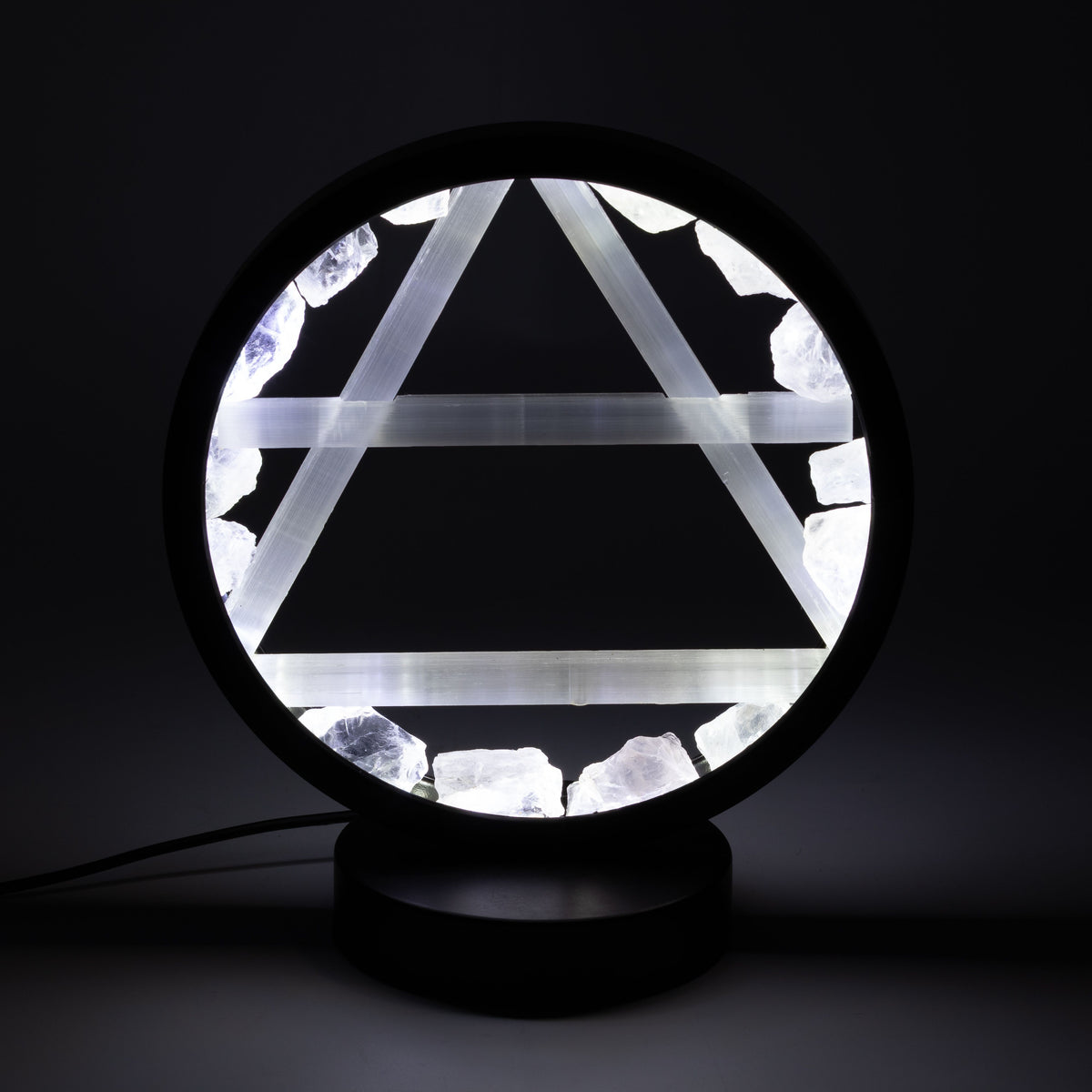 A circular black table lamp with a glowing white geometric triangle design and rough white crystal-like accents, shown on a dark background.
